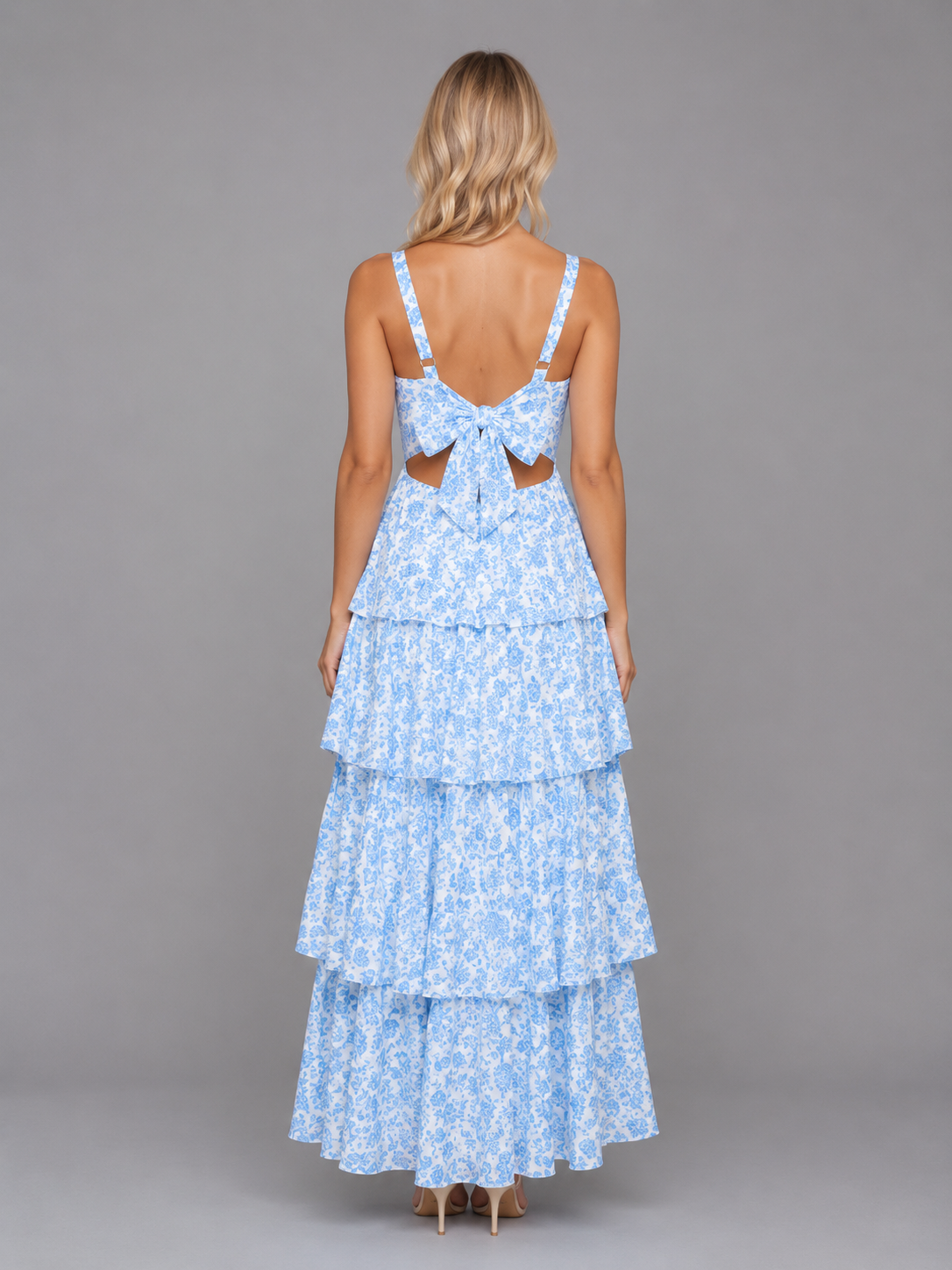 Woman wearing light blue floral tiered maxi dress with bow back detail and strappy shoulders, shown from behind