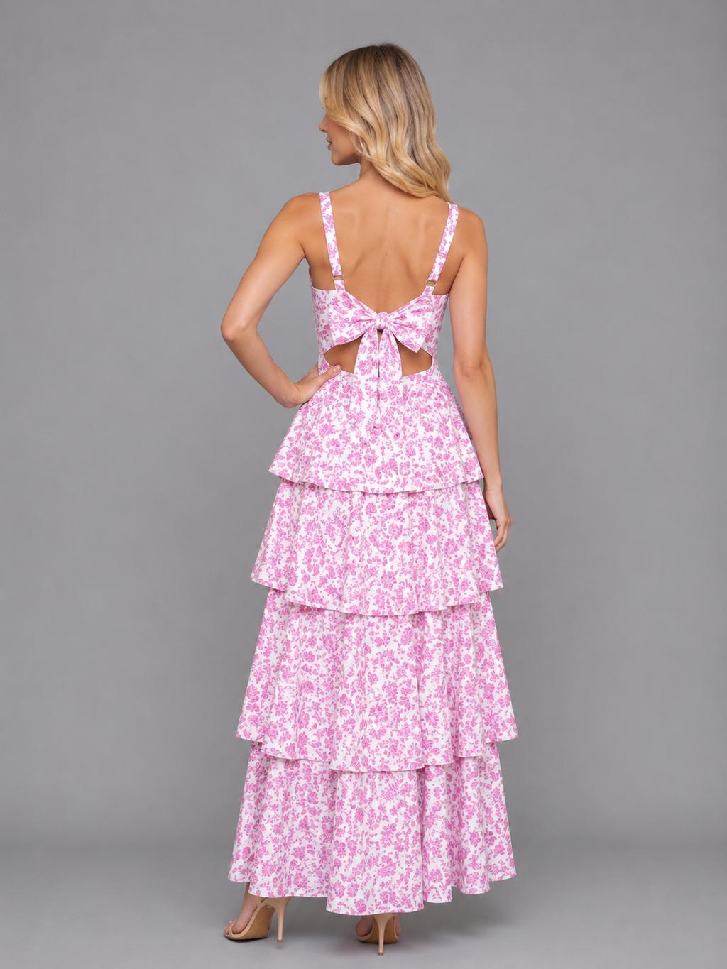 Woman wearing pink floral tiered maxi dress with bow back cutout detail and strappy neckline from behind