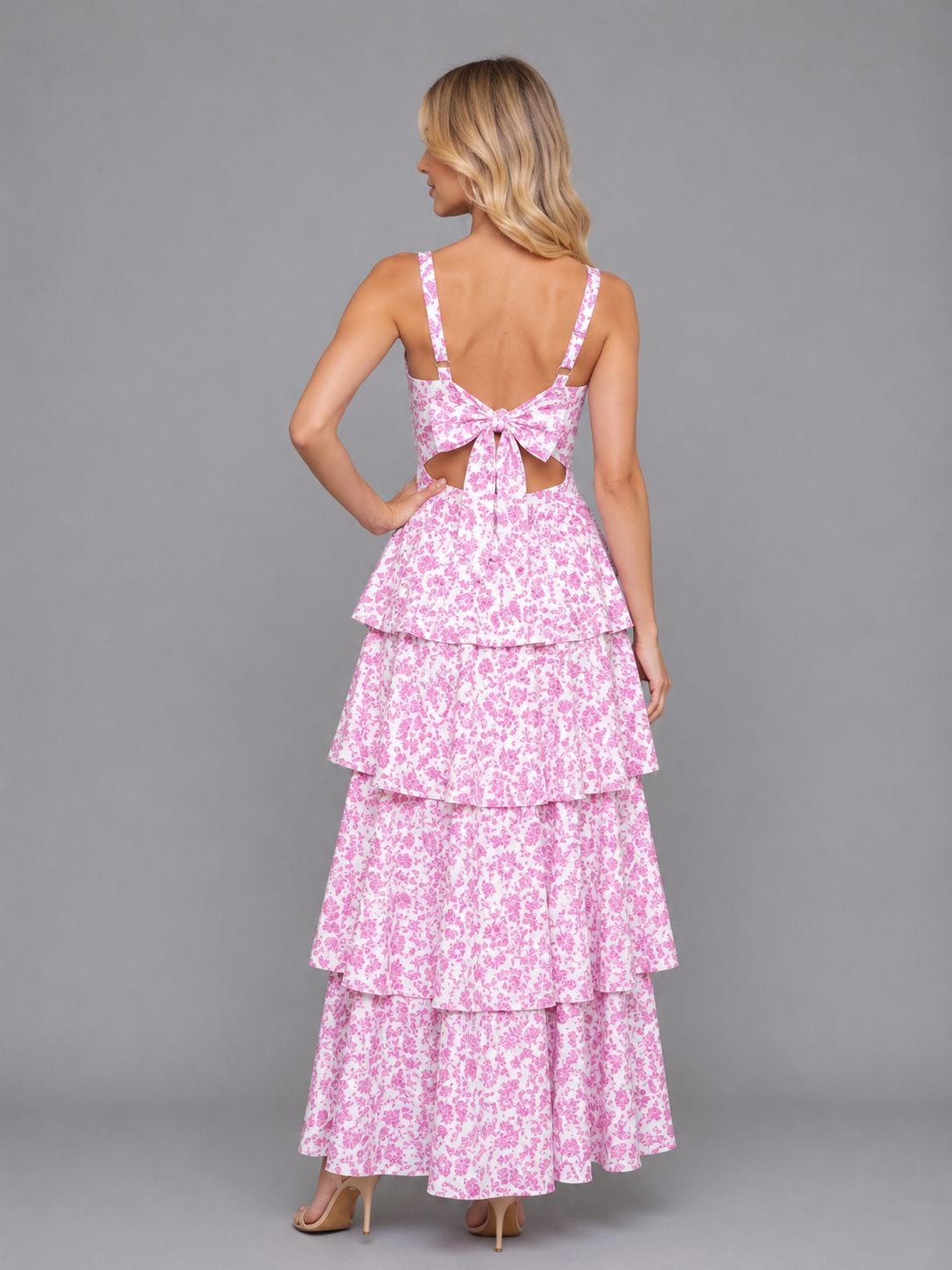 Woman wearing pink floral tiered maxi dress with bow back cutout detail and strappy neckline from behind
