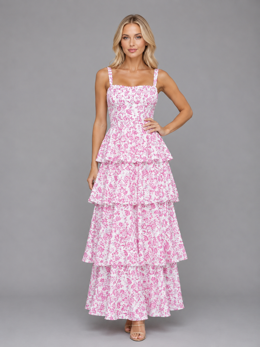 Woman wearing pink floral tiered maxi dress with square neckline and adjustable straps on gray background