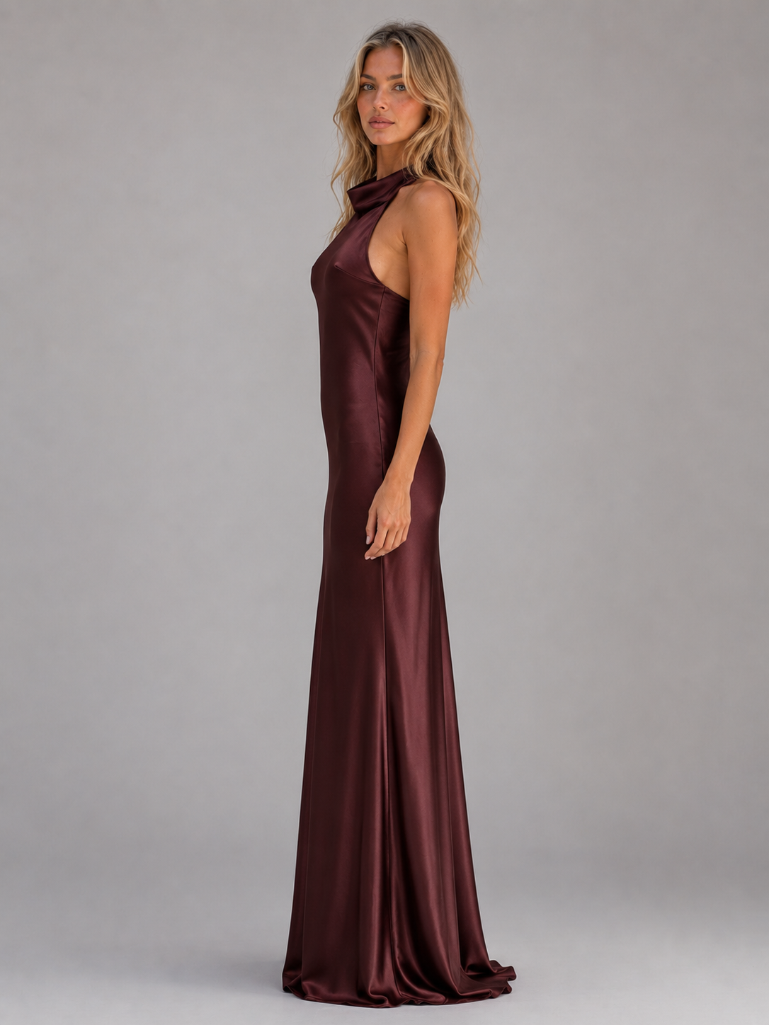 Woman wearing burgundy sculpted satin halter neck maxi dress with flowing skirt, shown in side profile against neutral background