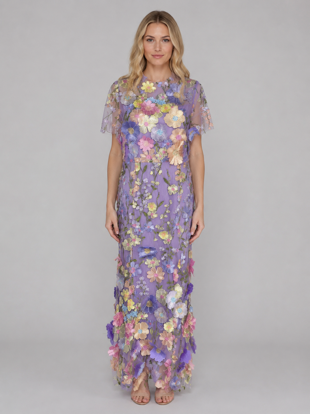Woman wearing lavender tulle maxi dress with colorful 3D floral embroidery throughout, short sleeves, floor-length hem