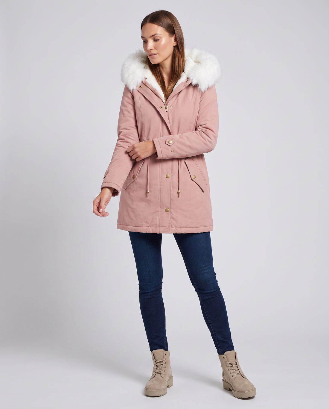 Woman wearing pink hooded winter parka with white fur trim, navy jeans, and beige lace-up boots