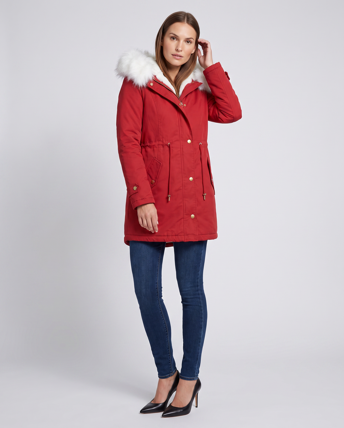 Woman wearing red winter parka with white fur-trimmed hood, dark blue jeans, and black heels