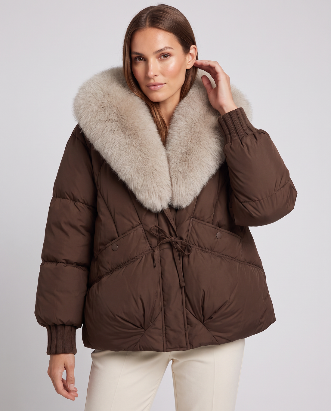 Woman wearing brown puffer jacket with cream faux fur collar and ribbed cuffs, paired with cream pants