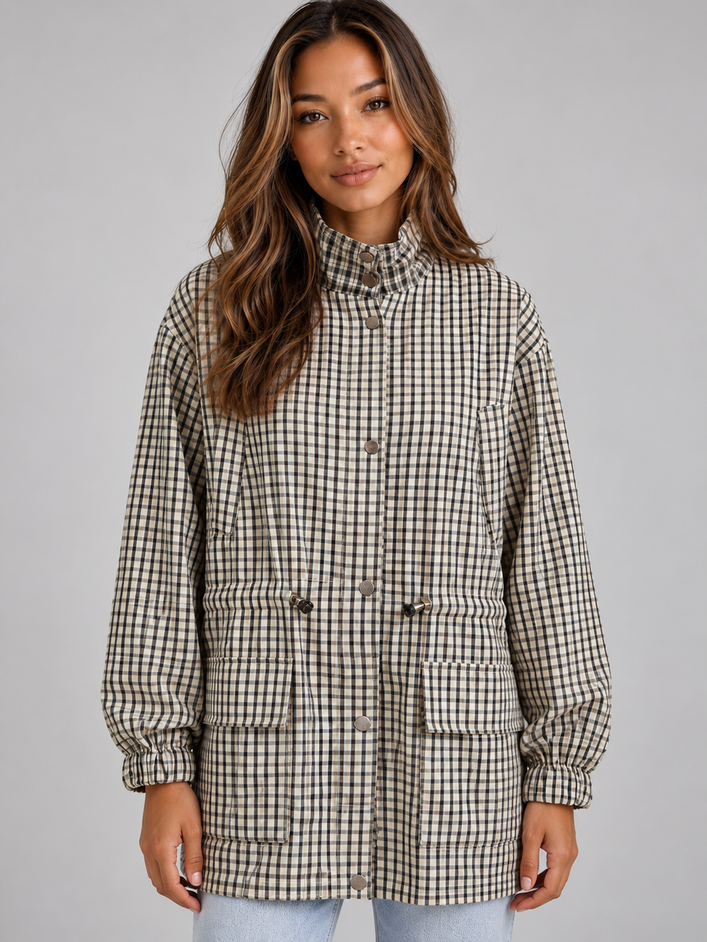 Woman wearing black and white gingham checked utility field coat with high neck, drawstring waist, and front pockets