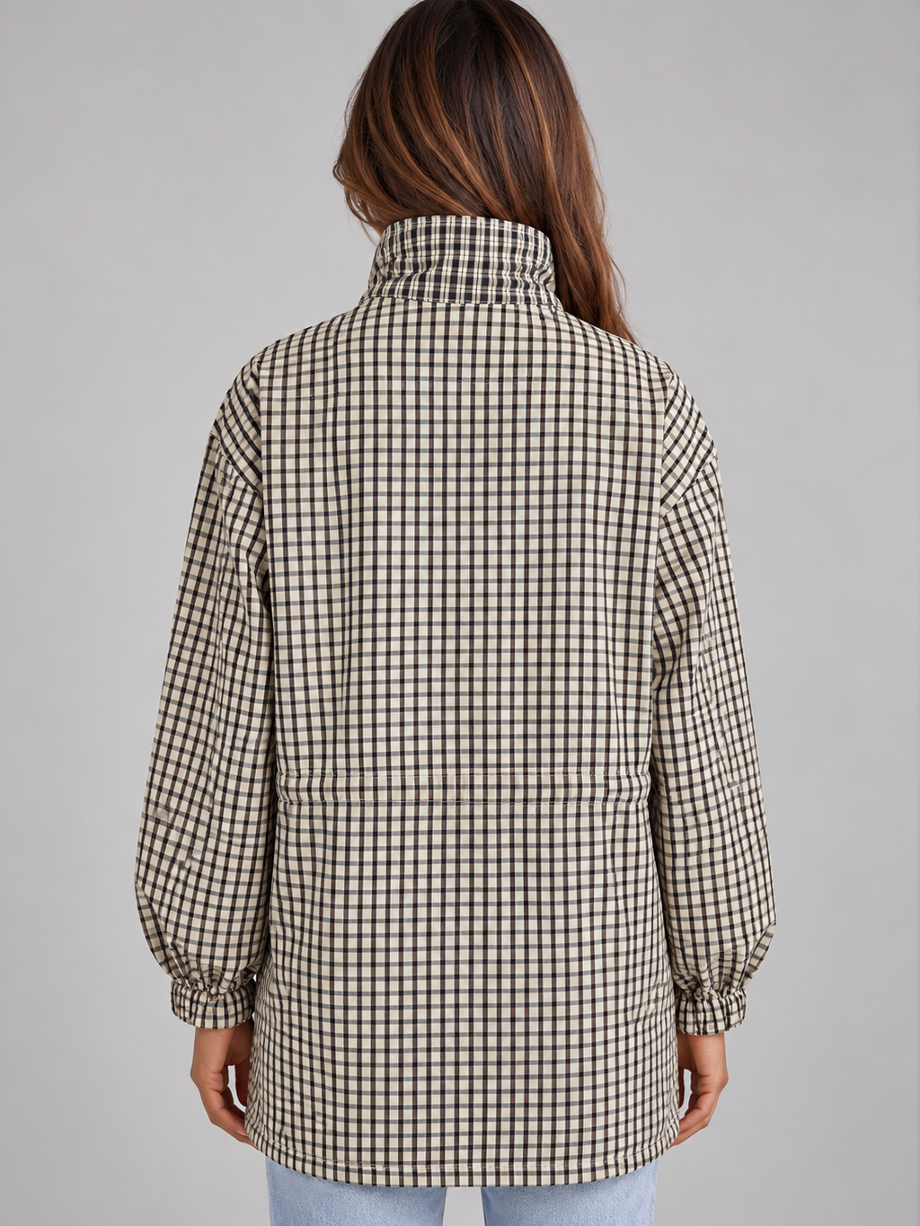 Woman wearing black and white checkered field coat with high neck and drawstring, shown from back view