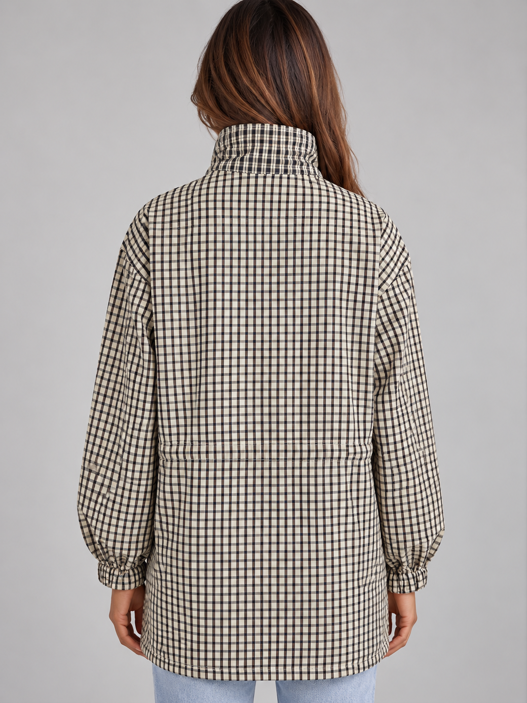 Woman wearing black and white checkered field coat with high neck and drawstring, shown from back view