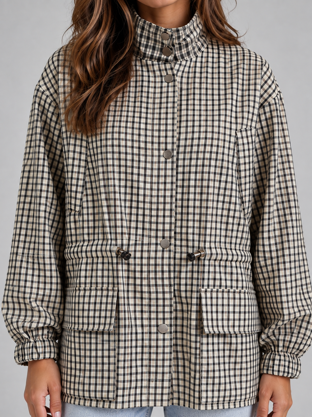 Woman wearing black and white checkered utility jacket with high neck, drawstring waist, and button front closure