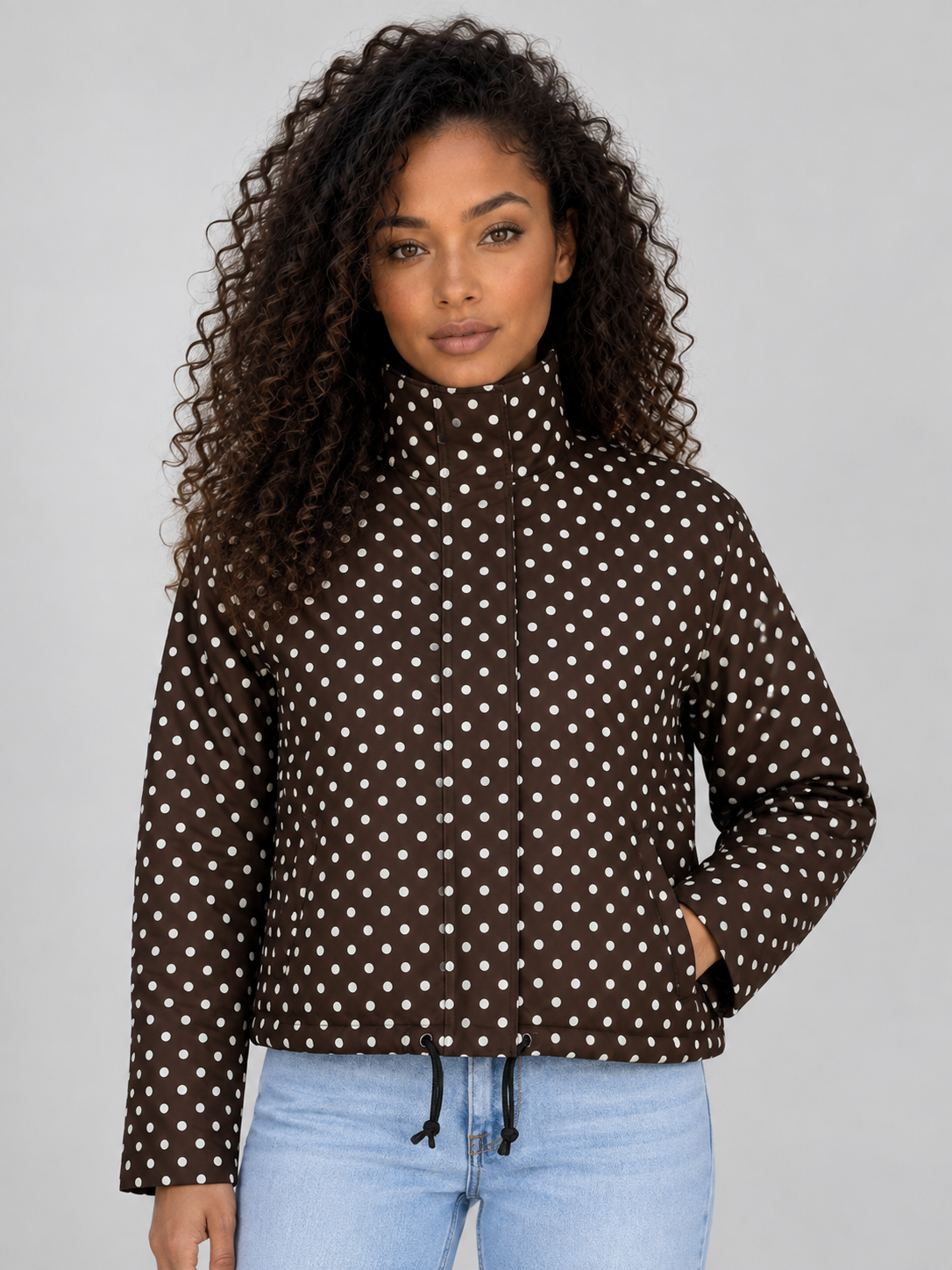 Woman wearing brown polka dot high collar cropped zip up jacket with drawstring and light blue jeans