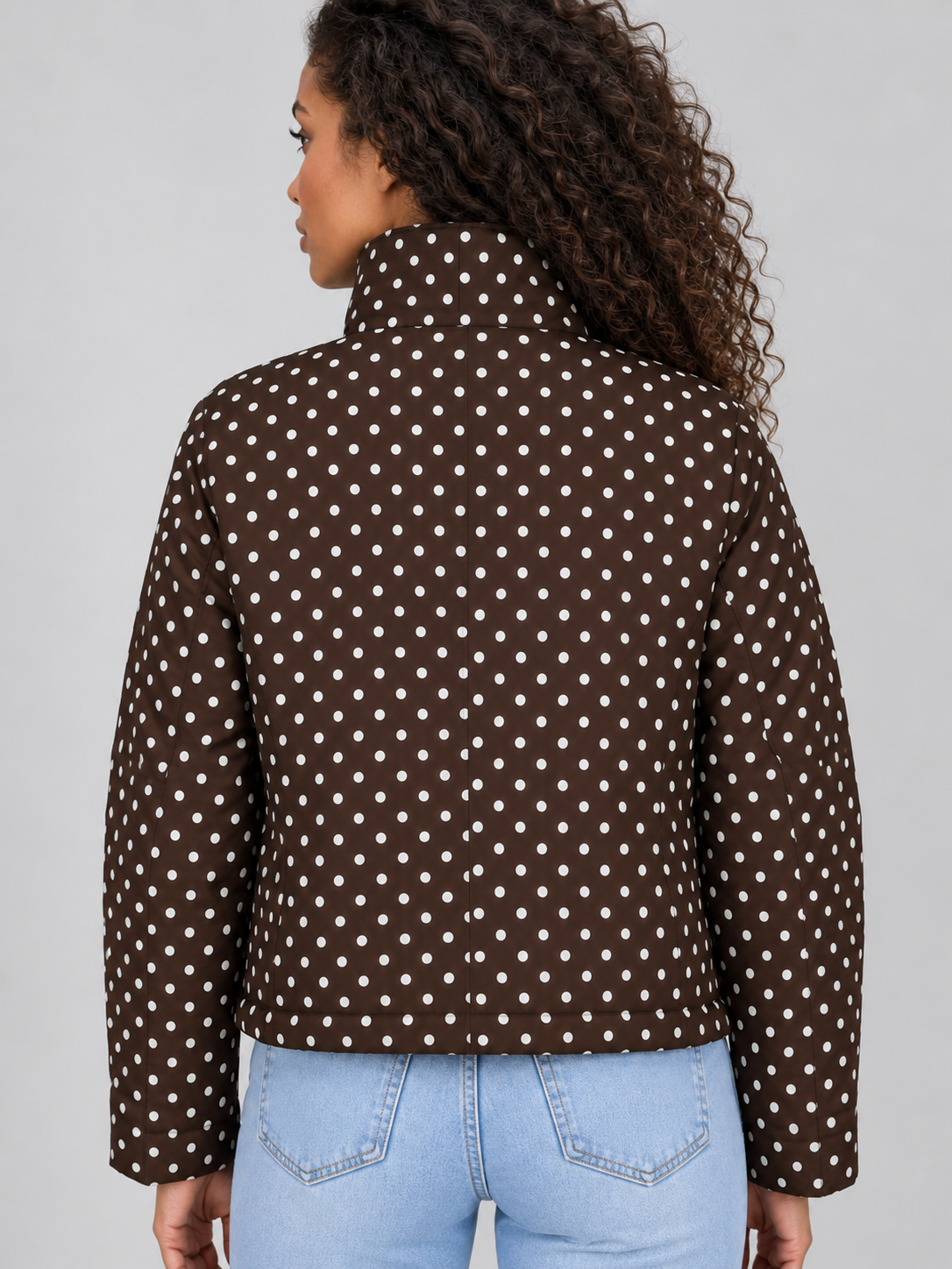 Woman wearing brown polka dot cropped zip up jacket with high collar, shown from back, paired with light blue jeans
