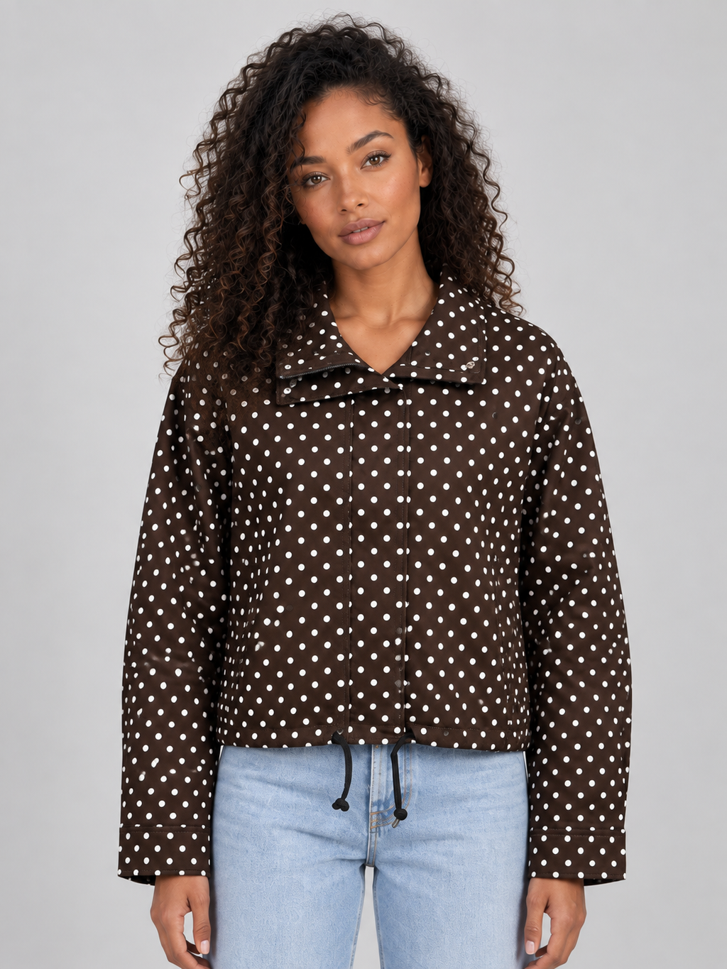 Women's brown polka dot cropped zip-up jacket with high collar and drawstring worn with light blue jeans