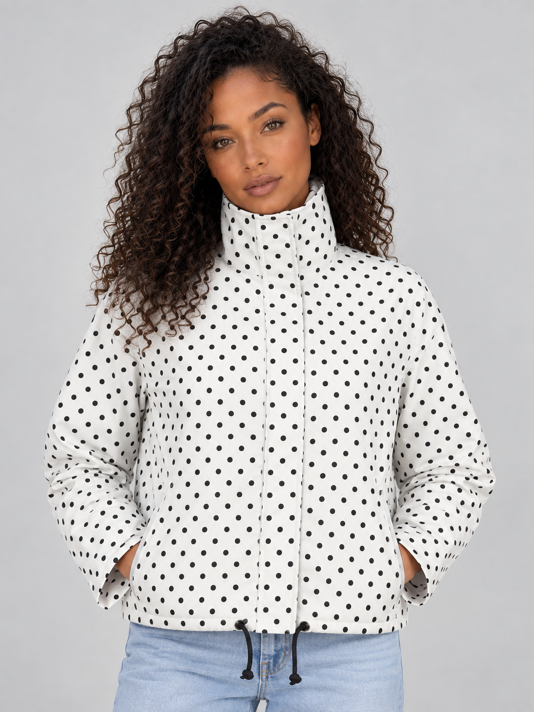 Woman wearing white polka dot cropped zip-up jacket with high collar and drawstring, paired with light blue jeans