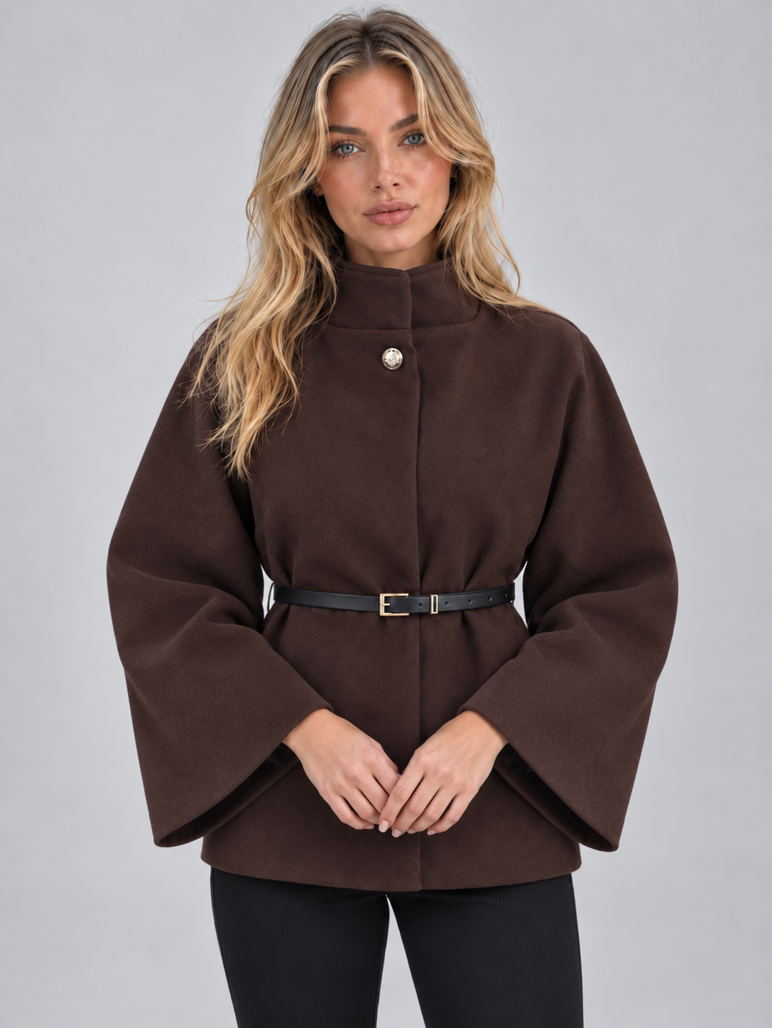 Woman wearing roux brown high neck belted cape jacket with flared sleeves and black pants