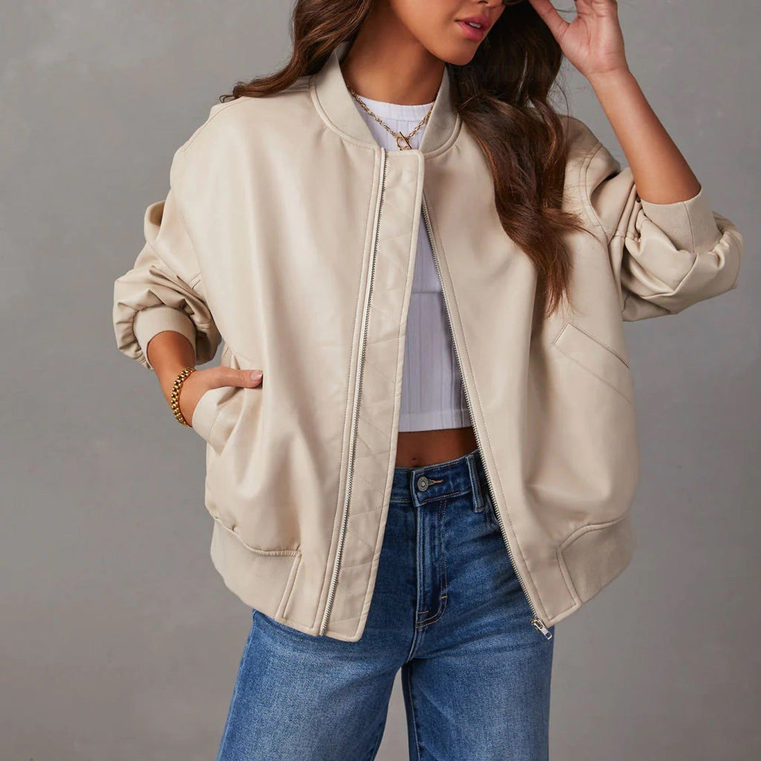 Woman wearing cream-colored leather bomber jacket with zipper, lavender crop top, and blue jeans