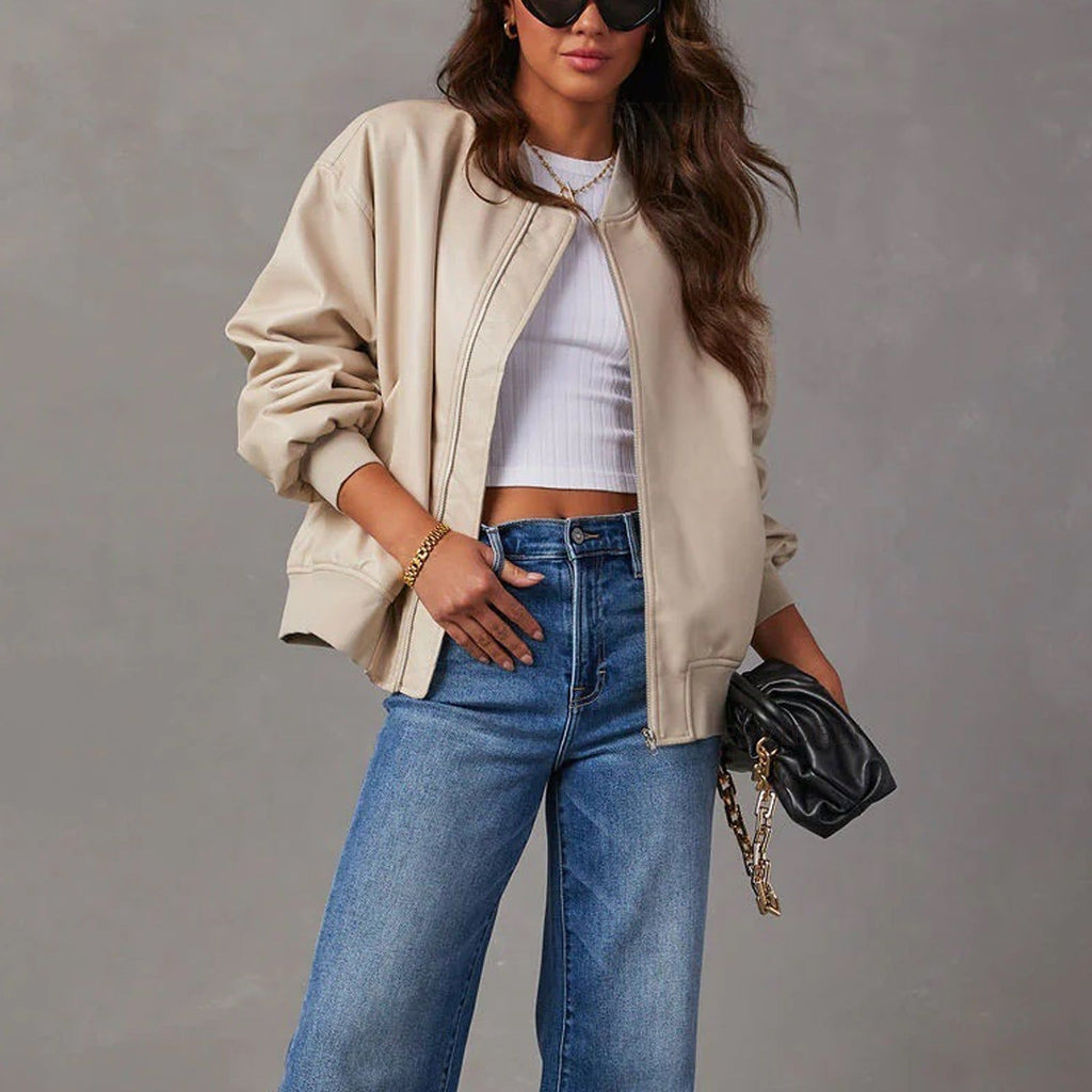 Woman wearing beige leather jacket, white ribbed crop top, and blue jeans with black quilted crossbody bag and sunglasses