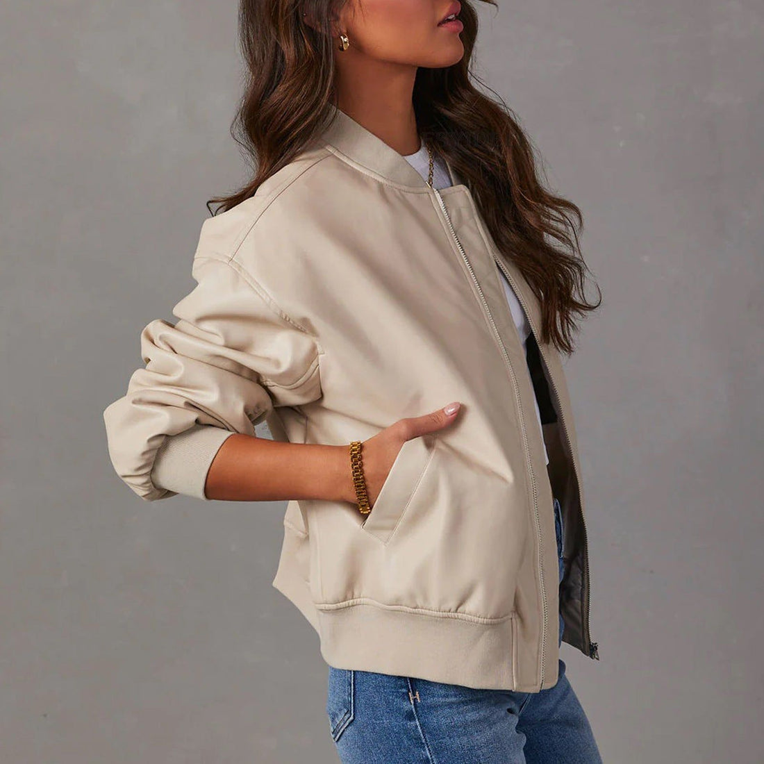 Woman wearing cream leather jacket over white shirt with blue jeans, showcasing front zip closure and side pockets