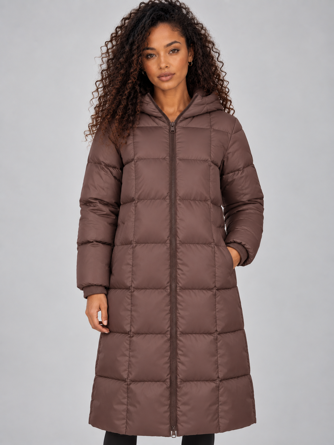 Woman wearing a brown padded puffer jacket with hood, full zip front, and ribbed cuffs, styled with black pants