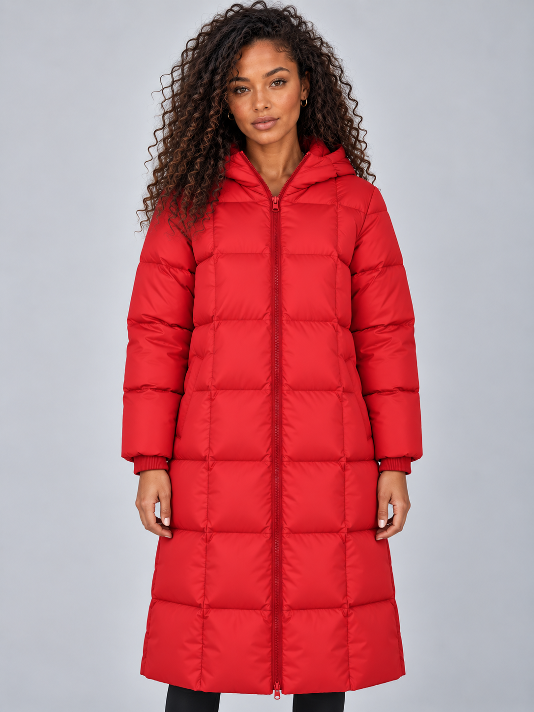 Woman wearing red padded full zip hooded puffer winter jacket with long length, paired with black pants