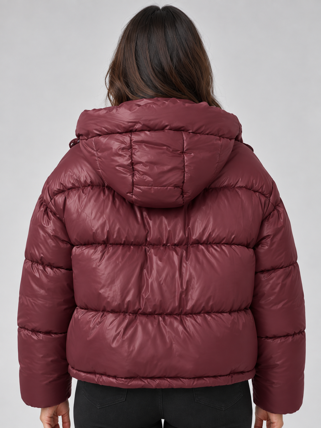Woman wearing burgundy padded puffer hooded winter jacket with full zip, shown from back view against gray background