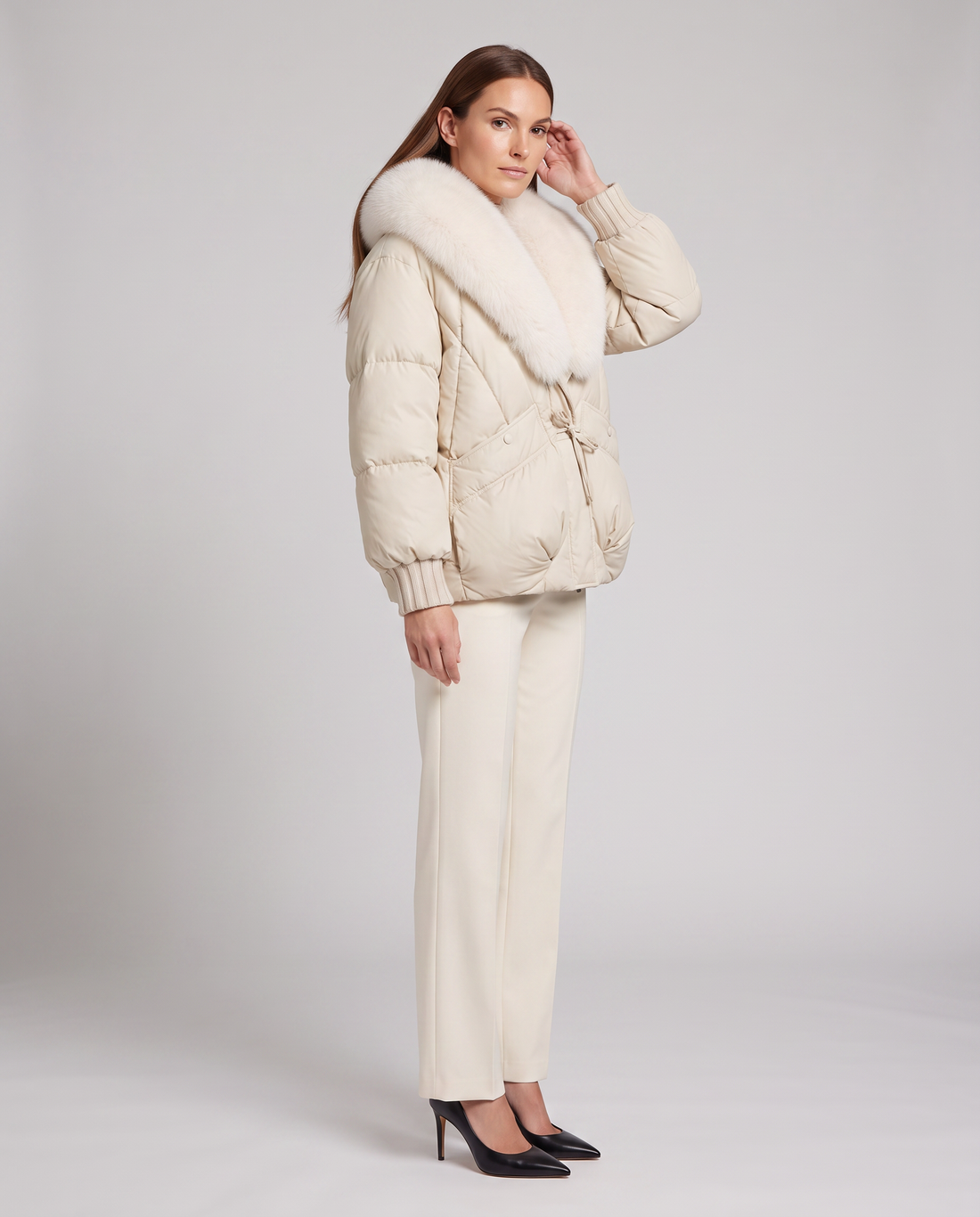 Woman wearing beige padded puffer jacket with white fur collar and cream trousers with black heels