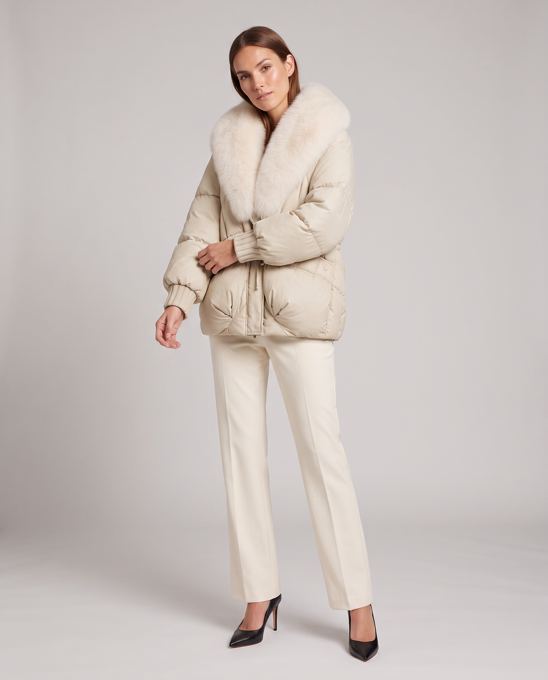Woman wearing beige padded puffer jacket with oversized fur collar, matching trousers and black pointed heels
