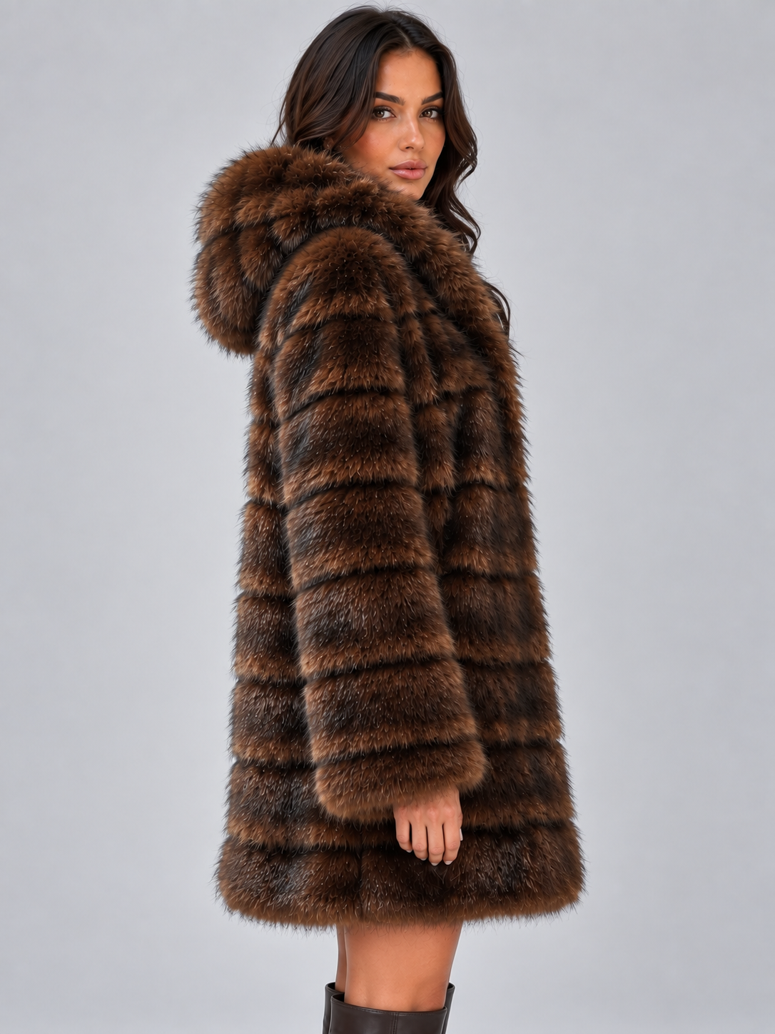 Woman wearing brown plush panelled faux fur hooded coat with horizontal striped design, shown from back view against white background