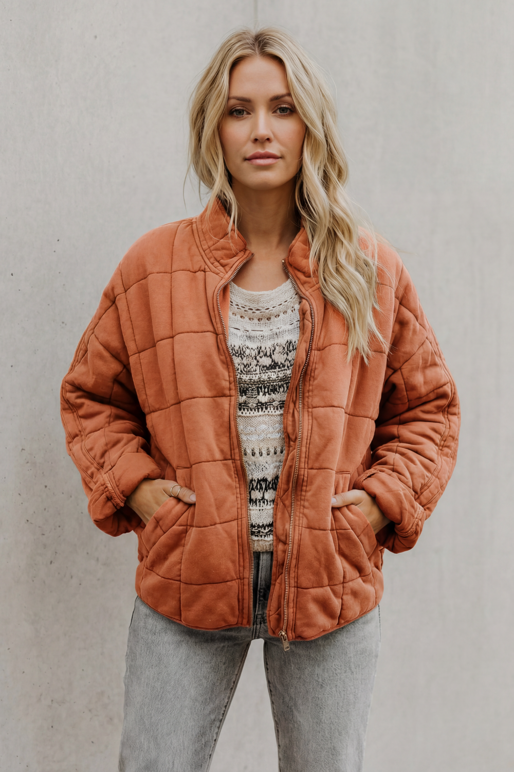 Woman wearing rust orange quilted jacket with high collar over patterned knit sweater and gray pants