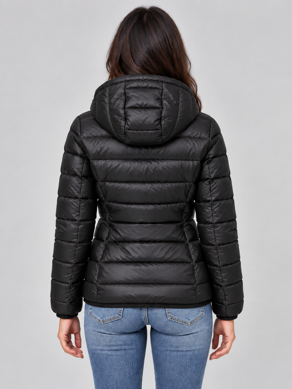 Woman wearing black quilted zip-up hooded puffer jacket with light blue jeans, back view