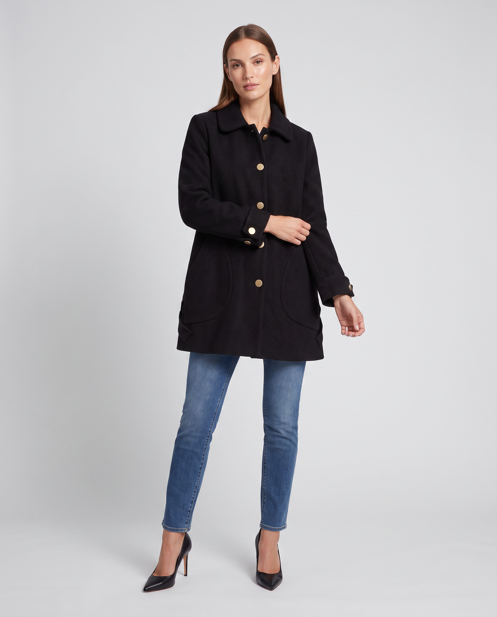 Woman wearing black round collar mid-length oversized coat with gold buttons over blue jeans and black heels