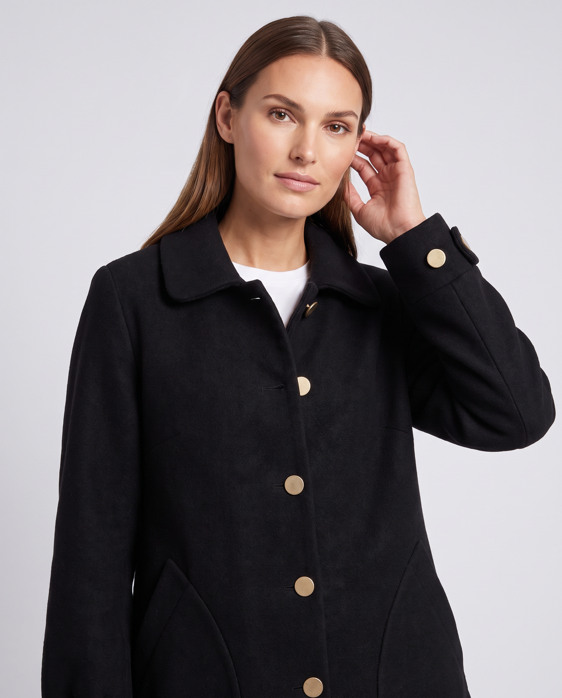 Woman wearing black oversized mid-length coat with round collar and gold buttons over white shirt