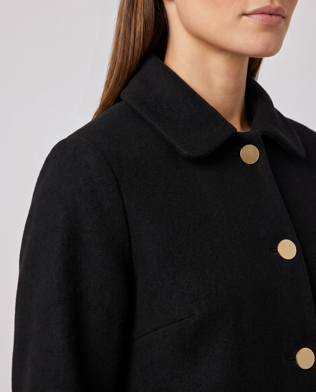 Woman wearing black oversized coat with round collar and gold circular buttons, viewed from chest up in profile