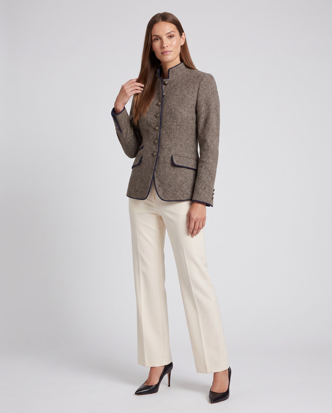 Woman wearing brown stand collar tailored blazer with cream pants and black heels, front view