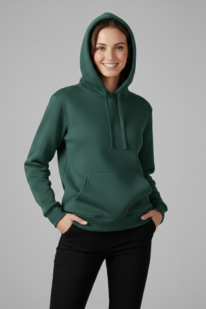 Woman wearing dark green hoodie with adjustable drawstring hood and ribbed hem, paired with black pants, standing against gray background