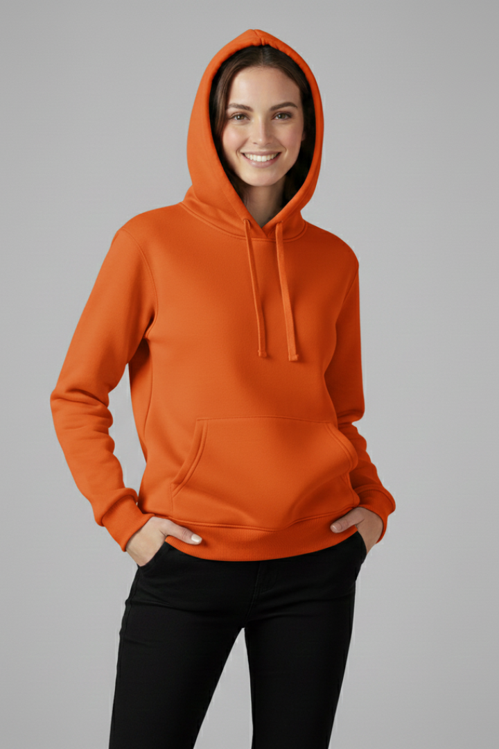 Woman wearing orange adjustable hood hoodie with ribbed hem and black pants, standing against gray background